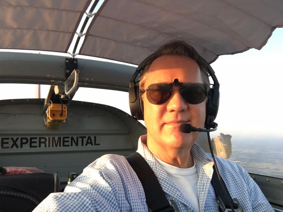 Daniel at the controls in flight, headset on, the horizon out the canopy beside him.
