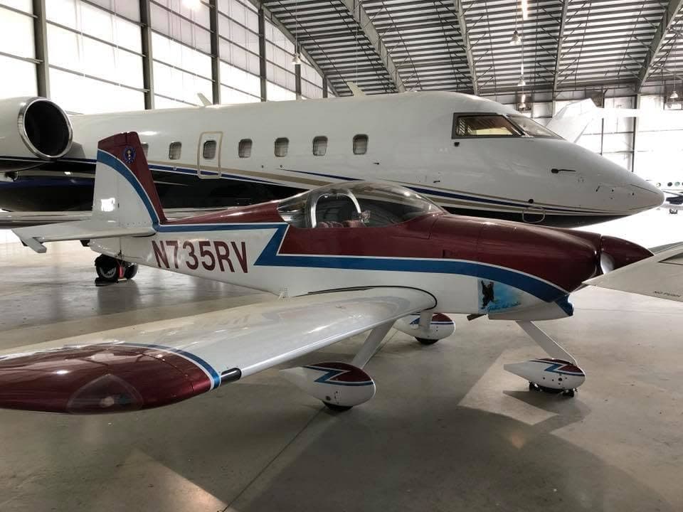 Daniel's RV, N735RV, in maroon and blue trim, parked in a hangar beside a business jet.